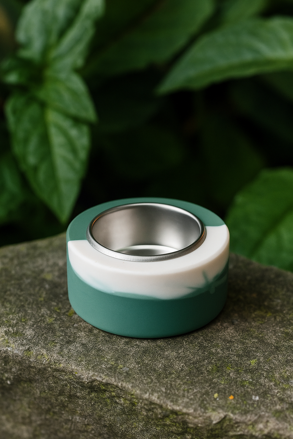 Green and white ceramic dish with metallic interior on a stone surface with green foliage in the background